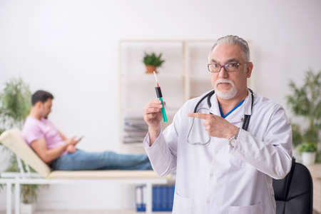 Old male doctor and young male patient in vaccination conceptの写真素材