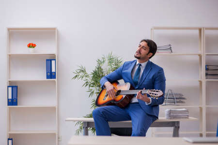 Young male employee playing guitar at workplaceの写真素材