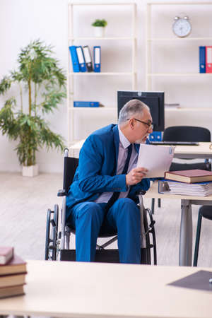 Old male employee in wheel-chair sitting in the officeの写真素材