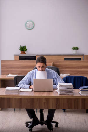 Young male employee and too much work in the officeの写真素材