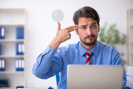 Young male employee unhappy with excessive work in the officeの写真素材