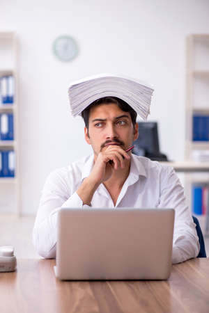 Young male employee and too much work in the officeの写真素材