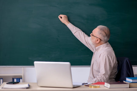 Old male teacher in front of blackboard