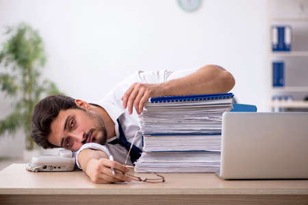 Young male employee unhappy with excessive work in the officeの写真素材