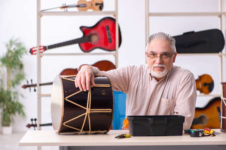 Old male repairman repairing musical instruments at workplace