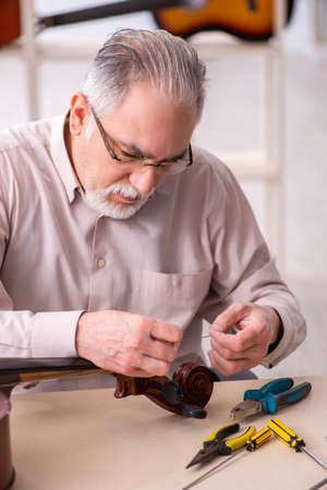 Old male repairman repairing musical instruments at workplaceの写真素材