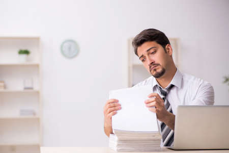 Young male employee unhappy with excessive work in the officeの写真素材