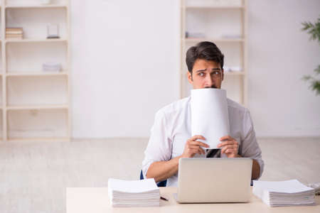 Young male employee unhappy with excessive work in the officeの写真素材