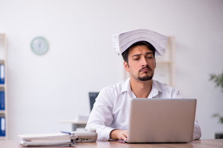 Young male employee and too much work in the officeの写真素材