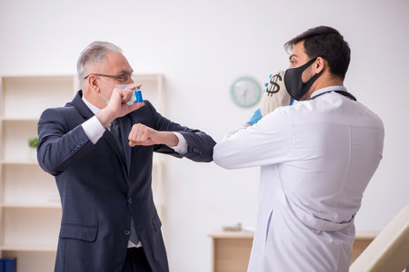 Old businessman visiting young male doctor in vaccination concepの写真素材
