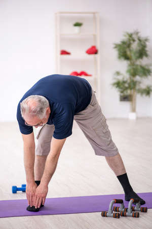 Old man doing sport exercises indoorsの写真素材
