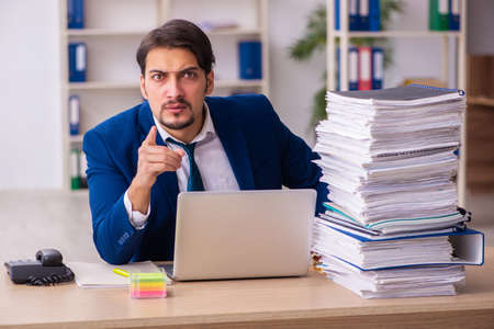 Young male employee and too much work in the officeの写真素材
