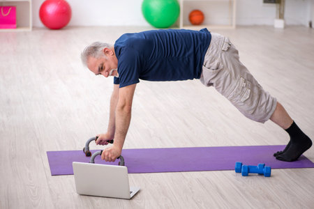 Old man doing sport exercises indoorsの写真素材