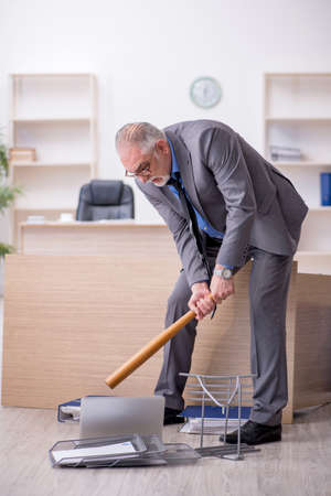 Old male employee holding baseball bat in the officeの写真素材