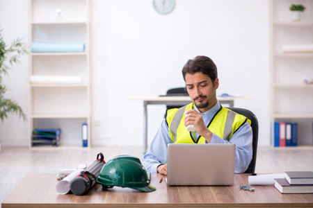 Tired young male architect drinking coffee during breakの写真素材