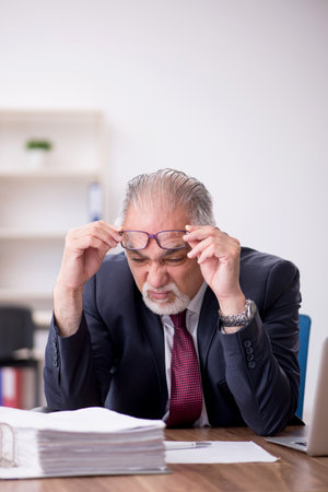 Old male employee and too much work in the officeの写真素材