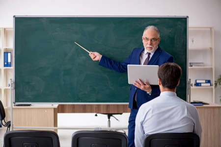 Old male teacher and young male student in front of green board