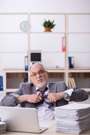 Old male employee unhappy with excessive work in the officeの写真素材