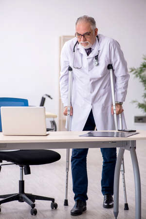 Leg injured old male doctor working in the clinicの写真素材