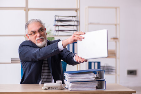 Old male employee unhappy with excessive work in the officeの写真素材