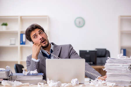 Young male employee and too much work in the officeの写真素材