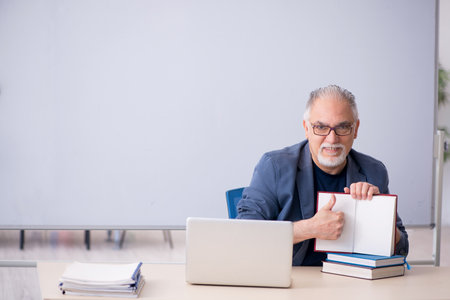 Old male teacher holding book in the classroomの写真素材