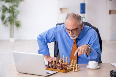 Old businessman playing chess at workplaceの写真素材