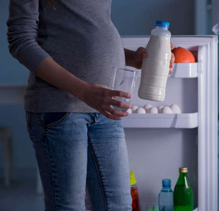 Pregnant woman near fridge looking for food and snacks at nightの写真素材