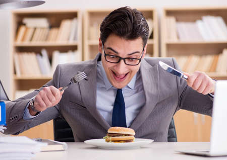 Hungry funny businessman eating junk food sandwichの写真素材