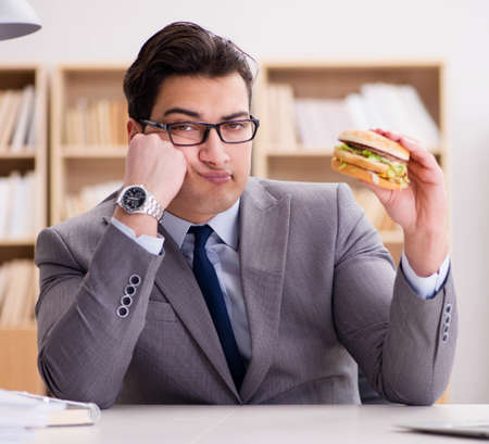 Hungry funny businessman eating junk food sandwichの写真素材