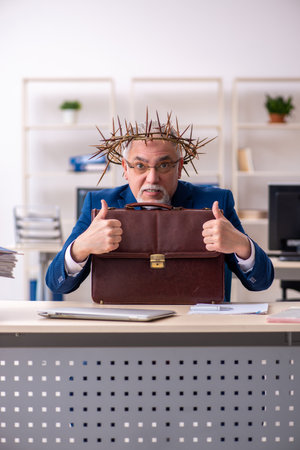 Old male employee wearing prickly wreath on headの写真素材