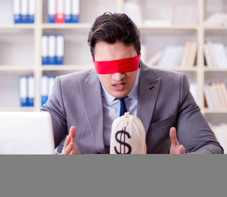Blindfold businessman sitting at desk in officeの写真素材