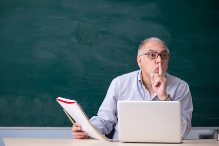 Old male teacher in front of green boardの写真素材