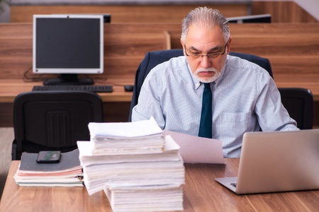 Old male employee and too much work in the officeの写真素材