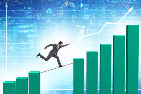 Businessman walking on tight rope between bar chartの写真素材