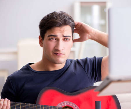 Young man practicing playing guitar at homeの写真素材