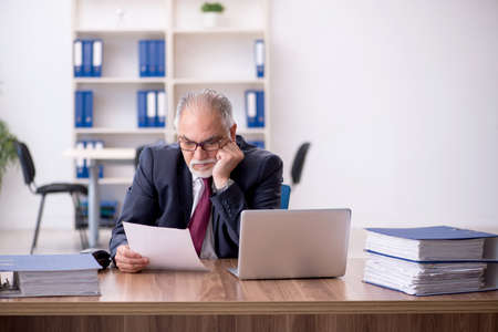 Old male employee and too much work in the officeの写真素材