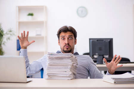 Young male employee and too much work in the officeの写真素材