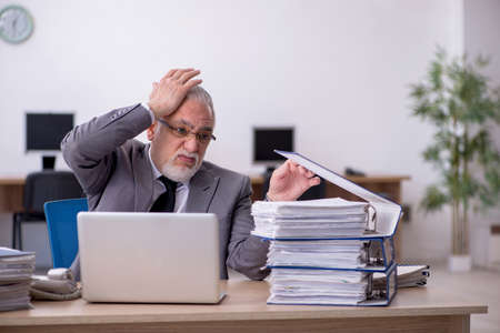 Old male employee unhappy with excessive work in the officeの写真素材