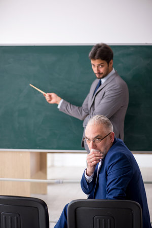 Young male employee and old boss in front of blackboardの写真素材