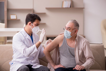 Young male doctor visiting old patient in vaccination conceptの写真素材
