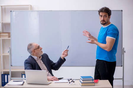 Old male teacher and young male student in front of whiteboardの写真素材