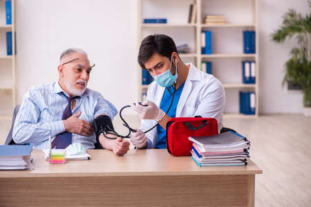 Young male doctor visiting old businessman at workplaceの写真素材