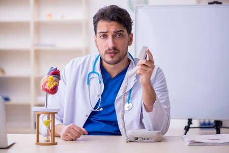Young male doctor cardiologist in time management conceptの写真素材