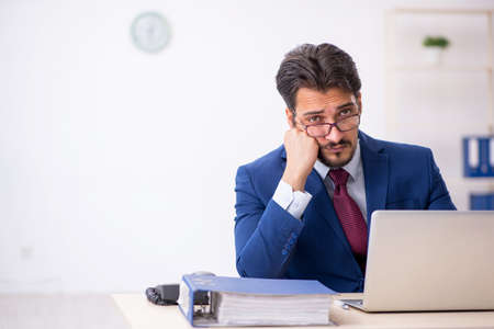 Young male employee unhappy with excessive work in the officeの写真素材