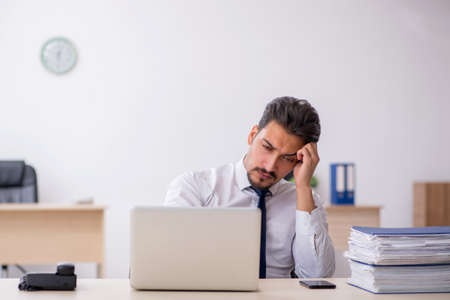Young male employee and too much work in the officeの写真素材