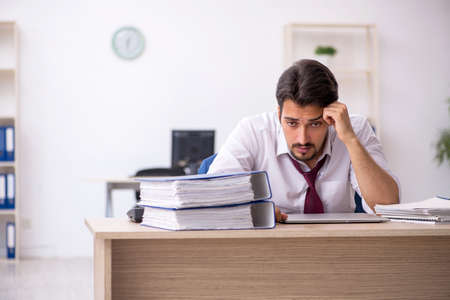 Young male employee unhappy with excessive work in the officeの写真素材