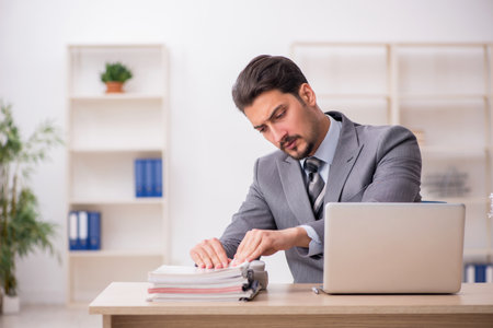 Young male employee unhappy with excessive work in the officeの写真素材