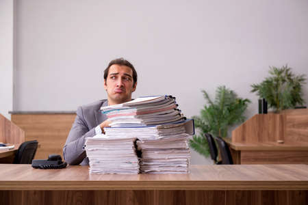 Young male employee unhappy with excessive work in the officeの写真素材