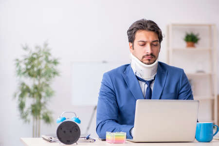 Young male employee after accident sitting at workplaceの写真素材